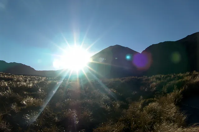 The sun rises up above Ngauruhoe's mountain side blinding hikers as they approach