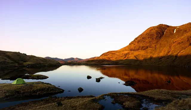 Stunning early morning vista of Stickle Tarn and the orange sun hitting Harrison Stickle