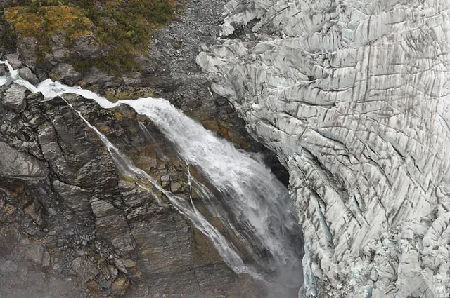 A flyby past a spectacular waterfall plunging beneath the glacier